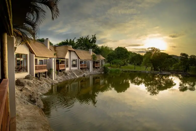 Lodge de safari luxueux au coucher du soleil se reflétant sur un lac tranquille dans le parc Kruger, parfait pour une escapade faunique.